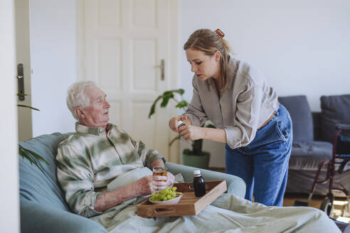 Healthcare worker giving medicine to man sitting with food in tray at home - HAPF03300