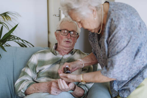 Senior woman giving medicine to man sitting on sofa at home - HAPF03307