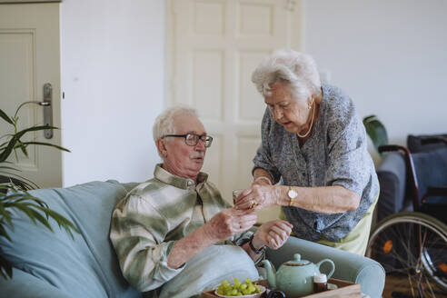 Ältere Frau serviert einem Mann, der zu Hause auf dem Sofa sitzt, ein Glas Wasser - HAPF03308