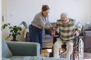 Mitarbeiter des Gesundheitswesens hilft einem älteren Mann, der zu Hause im Rollstuhl sitzt - HAPF03314