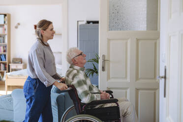 Smiling healthcare worker with man sitting in wheelchair at home - HAPF03315