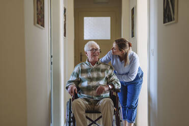 Glückliche Pflegekraft im Gespräch mit einem älteren Mann, der zu Hause im Rollstuhl sitzt - HAPF03319