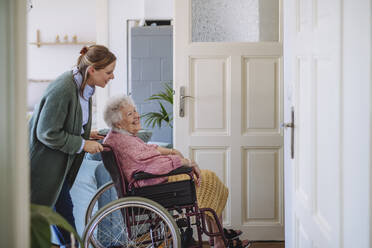 Gesundheitspflegerin mit älterer Frau, die zu Hause im Rollstuhl sitzt - HAPF03324