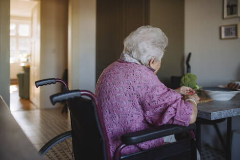 Ältere Frau sitzt im Rollstuhl am Tisch - HAPF03333
