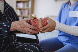 Mitarbeiter des Gesundheitswesens überreicht Geschenk an älteren Mann zu Hause - HAPF03353