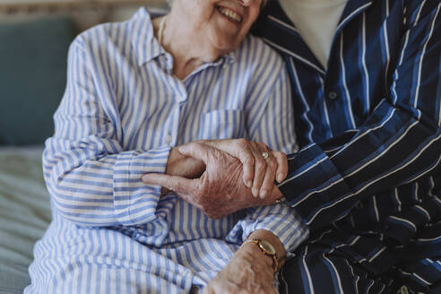 Glückliche ältere Frau hält Hände mit Mann auf dem Bett zu Hause sitzen - HAPF03364