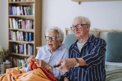 Ältere Frau strickt mit Mann, der die Fernbedienung hält und zu Hause fernsieht - HAPF03365