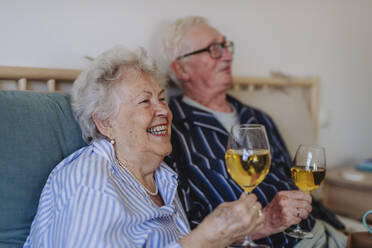 Glückliche ältere Frau und Mann mit Weingläsern auf dem Bett zu Hause - HAPF03369