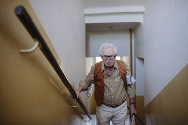Senior man standing on staircase at home - HAPF03378