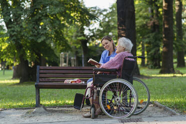 Glückliche Mitarbeiterin im Gesundheitswesen mit älterer Frau im Rollstuhl sitzend im Park - HAPF03385