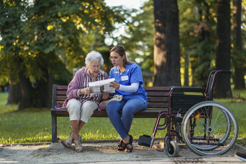 Gesundheitspflegerin mit älterer Frau, die im Park Zeitung liest - HAPF03391