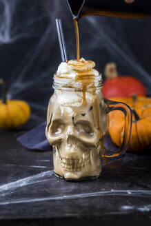 Sirup gießt auf einen totenkopfförmigen Becher mit Kürbisgewürz-Latte und Schlagsahne - SBDF04662