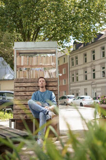 Mature man with eyes closed sitting near cabinet of books - KNSF09934