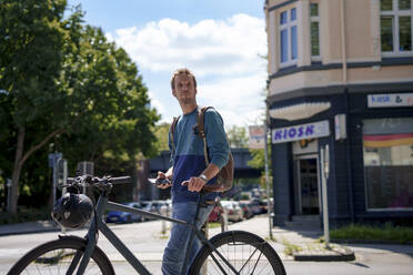 Älterer Mann hält Smartphone und steht mit Fahrrad an einem sonnigen Tag - KNSF09936