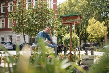 Mature man sitting in front of trees and building - KNSF09940