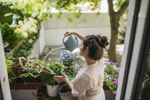 Woman watering flowers, taking care of plants on balcony - HAPF03403