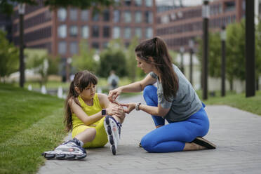 Mother helping daughter injuring herself roller skating at the city park - HAPF03415