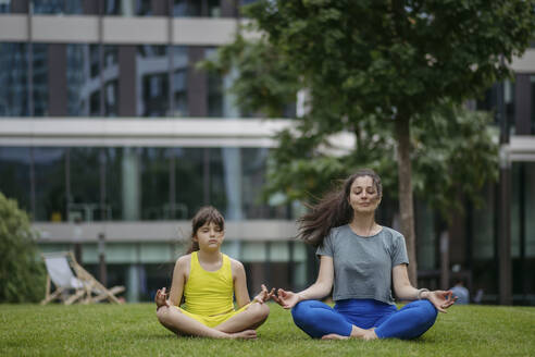 Mother and daughter spending together time outdoors practicing yoga in the city park - HAPF03417