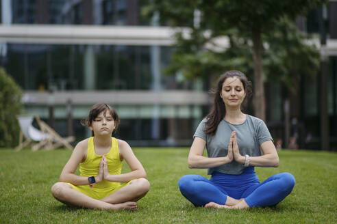Mother and daughter spending together time outdoors practicing yoga in the city park - HAPF03418