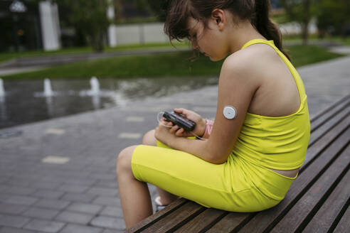 Mädchen mit Diabetes überprüft ihren Blutzuckerspiegel an einer Insulinpumpe und trägt einen CGM-Sensor - HAPF03421