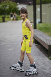 Mädchen mit Diabetes, das eine Insulinpumpe und einen CGM-Sensor trägt, beim Rollschuhlaufen im Stadtpark - HAPF03424