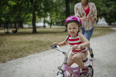 Little girl is learning to ride a bike in the city park wearing cycling helmet - HAPF03430