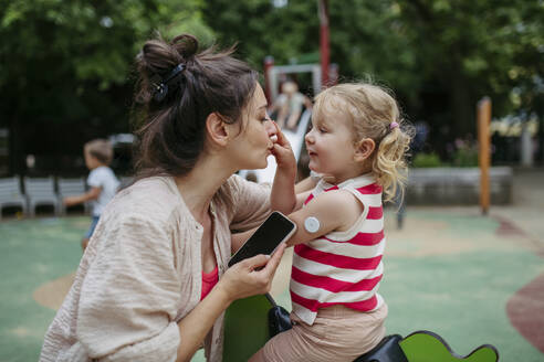 Mother with smartphone checking on little girl with a continuous glucose monitor sensor on her shoulder - HAPF03436