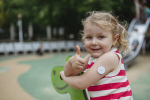 Little girl with diabetes giving thumbs up playing on seesaw on playground - HAPF03437