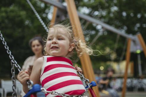 Little toddler girl and mother have fun at playground swinging on a swing - HAPF03441