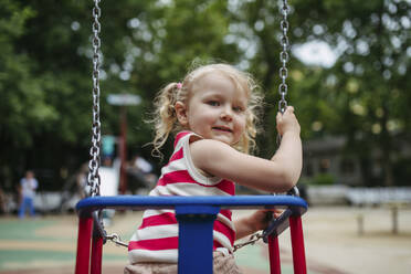 Smiling girl sitting in swing at gthe playground - HAPF03443