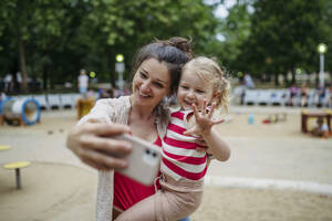 Little toddler girl and mother having fun at playground taking selfies with smartphone - HAPF03445