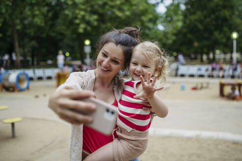 Little toddler girl and mother having fun at playground taking selfies with smartphone - HAPF03445