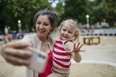 Little toddler girl and mother having fun at playground taking selfies with smartphone - HAPF03446