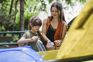 Mother and schoolgirl daughter separate waste into recycling bins in the city - HAPF03450