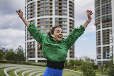 Beautiful woman exercises in a city park raising arms happily - HAPF03467