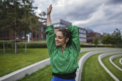 Schöne Frau trainiert in einem Stadtpark, läuft, dehnt sich und macht Atemübungen. Training in einem städtischen Fitnessbereich im Freien. - HAPF03469