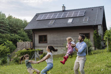 Young family having fun in front their family house with solar panels on the roof - HAPF03483