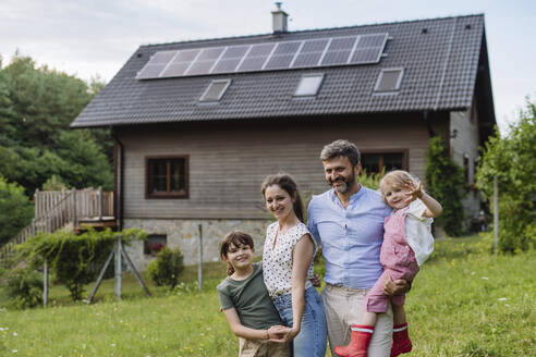 Happy family standing in front their family house with solar panels on the roof - HAPF03484