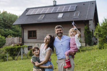 Young family having fun in front their family house with solar panels on the roof - HAPF03485