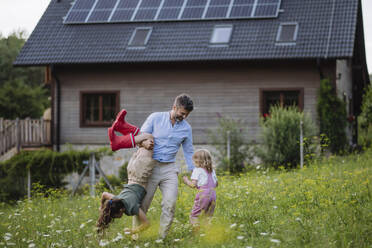 Father and daughters having fun in front their family house with solar panels on the roof - HAPF03489