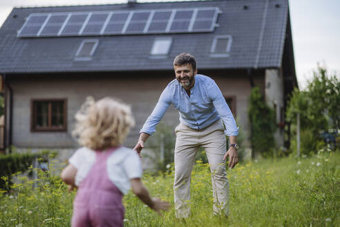 Lttle daughter running to father in front their family house with solar panels on the roof - HAPF03490