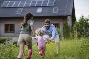 Father and daughters having fun in front their family house with solar panels on the roof - HAPF03491