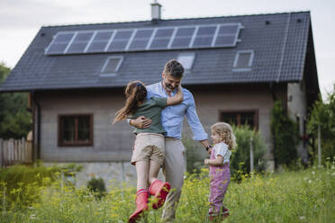 Father and daughters having fun in front their family house with solar panels on the roof - HAPF03492