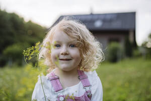 Cute little girl in front her family house holding flower - HAPF03500