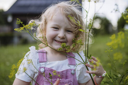 Cute little girl in front her family house holding flower - HAPF03501