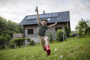 Little girl running in front her family house with solar panels on the roof holing windturbine model - HAPF03502