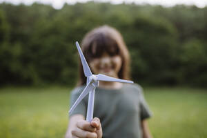 Girl standing in nature holding model of wind turbine - HAPF03504
