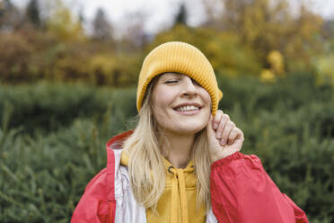 Smiling woman wearing raincoat and pulling knit hat - VBUF00491