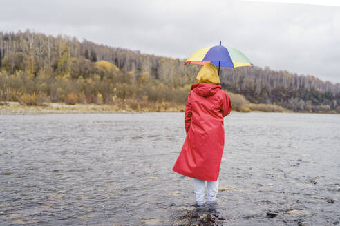 Frau in rotem Regenmantel und mit Regenschirm im Fluss stehend - VBUF00492