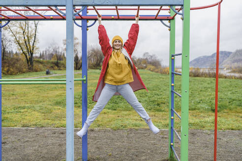 Lächelnde Frau, die an einem Affengitter im Park hängt - VBUF00497